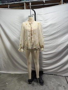 Detail of French style beige blouse featuring intricate floral embroidery and tie neck collar