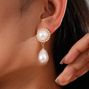 Detail shot of golden drop earrings with round and teardrop pearls on a female model