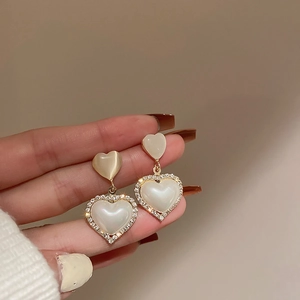 Macro detail of luxury heart pearl earrings with gold frame and micro-set cubic zirconia