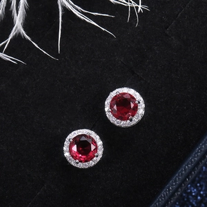 Detail view of round red gemstone stud earrings with white zircon halo on black velvet