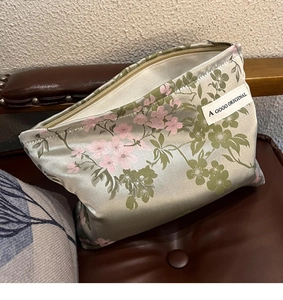 Detail of light green satin cosmetic bag with pink floral patterns on a leather chair