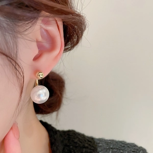 Close-up of elegant gold-plated pearl drop earring on model's ear showing shiny texture