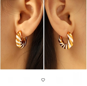 Close-up of twisted gold and white enamel hoop earrings worn on ears in split view