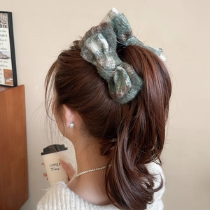 Close-up of a large tweed bow hair claw clip styled on a model in a cozy cafe setting