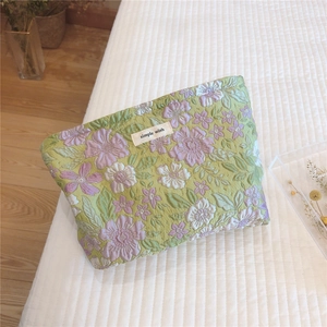 Detail of floral tapestry cosmetic bag with simple wish label on soft quilted texture
