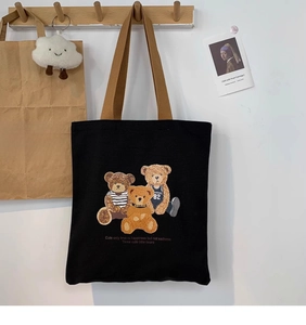 Detail of cute teddy bear embroidery on a black canvas tote bag with brown straps
