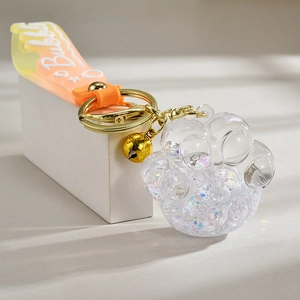 Close-up of cat paw acrylic keychain with orange strap, glitter, and gold bell detail