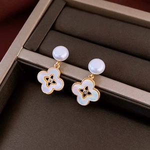 Detailed macro view of gold-plated mother of pearl clover earrings with white pearls