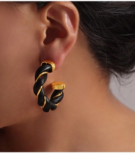 Close-up of C-shaped hoop earrings with twisted gold metal and black leather weave