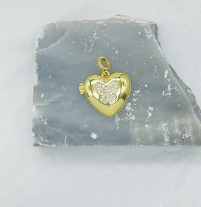 Detail showing a heart-shaped gold pendant with butterfly zircon inlay on rock background