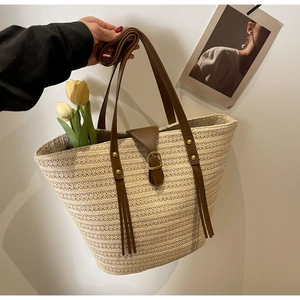 Close-up of woven straw tote bag with brown leather straps and vintage buckle detail