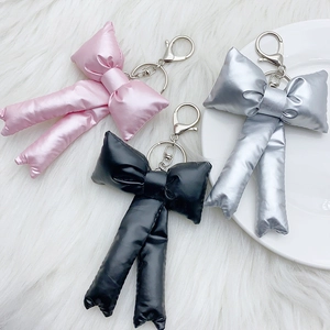 Three metallic padded bow keychains in pink, black, and silver with metal clasp rings