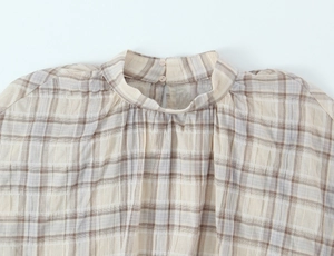 Detail of plaid pleated blouse featuring stand collar and double-button closure