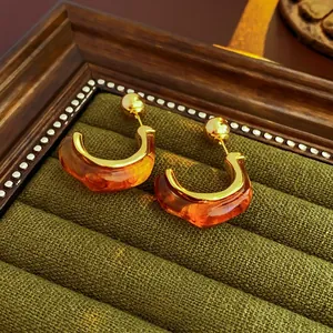 Detail of amber resin C-shape hoop earrings with gold metal trim on velvet display tray