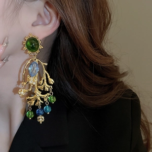 Détails macro des boucles d'oreilles pendantes en corail doré avec perles vertes et bleues