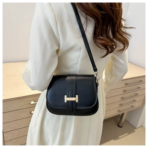 Detail of elegant black leather square bag with gold metal clasp on a textured background