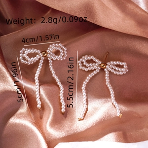 Macro shot of faux pearl bow earrings with golden beads on champagne silk fabric