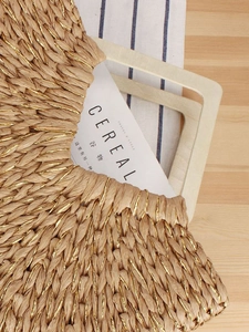Handwoven straw beach bag with gold thread accents and wooden handles on rustic background