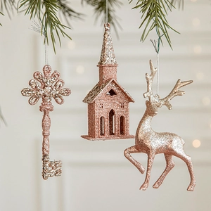 Rose gold glitter reindeer and house Christmas ornaments hanging on a pine tree branch