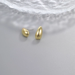 Macro shot of polished gold water drop earrings with silver pins on a grey background