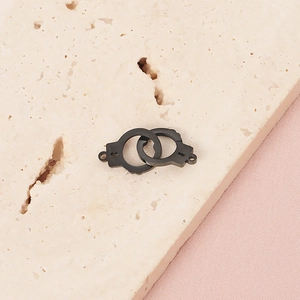 Macro shot of a black metal handcuff pendant on a stone slab with soft pink background