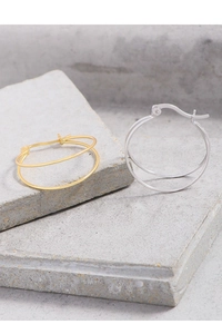 Close-up of interlocking double hoop earrings in gold and silver on stone base