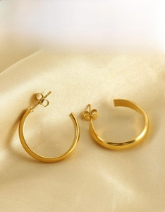 Detailed close-up of golden round hoop earrings on a champagne silk fabric background