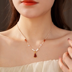 Detail of beaded pearl necklace featuring a red gourd pendant with gold accents