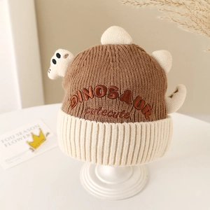 Close-up of knit dinosaur hat with 3D spikes and DINOSAUR embroidery on a white stand