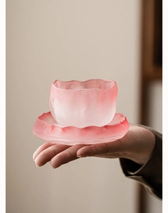 Close-up of a hand holding a pink frosted glass teacup with a unique wave-edged design