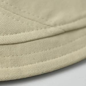 Close-up of the beige cotton bucket hat showing reinforced stitching and fabric texture