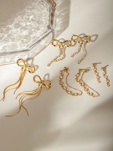 Detailed set of four gold tassel earrings with bows and zircon crystals on white surface