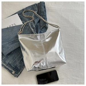 Silver metallic tote bag with chain strap displayed on white textured fabric background