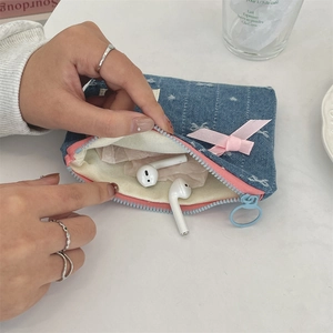Dettaglio del portamonete in denim con fiocco rosa, adatto per auricolari wireless