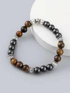 Men's Tiger Eye bead bracelet with metallic accents on a minimalist grey pedestal