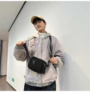 Detail of black canvas crossbody bag with multiple zippers worn with grey hoodie