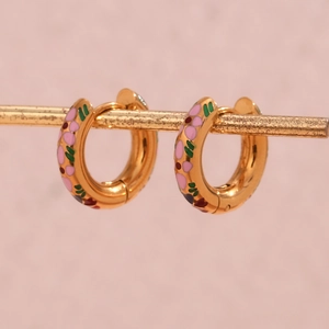 Close-up of gold hoop earrings featuring pink floral and green leaf enamel details