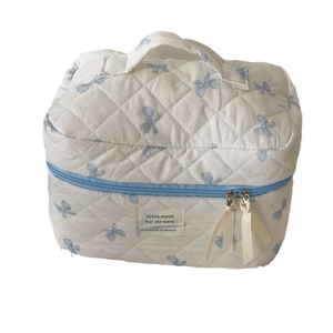 Quilted white cosmetic bag with blue bow patterns and a sturdy top handle for travel