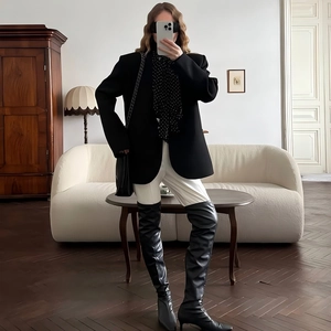 Detail of a loose-fit black blazer styled with a polka dot scarf and leather boots