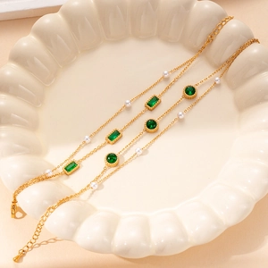 Elegant gold layered bracelet with green gemstones and white pearls on ceramic plate