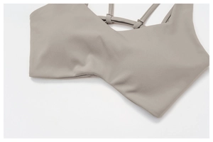 Detail shot of grey-brown sports bra showing thin criss-cross straps and adjustable buckles