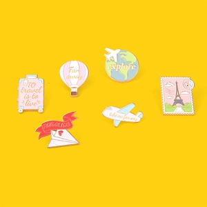 Close-up of travel themed metal enamel pins featuring suitcases and airplanes on yellow