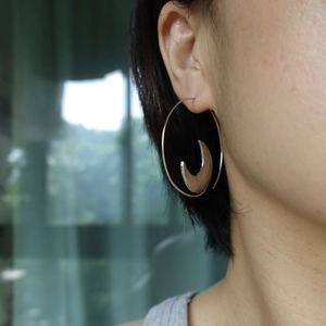 Close-up of silver sun and moon hoop earrings worn on ear showing modern metallic design