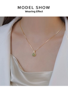 Détail d'un collier doré avec pendentif rond vert et nœud décoratif porté par un mannequin