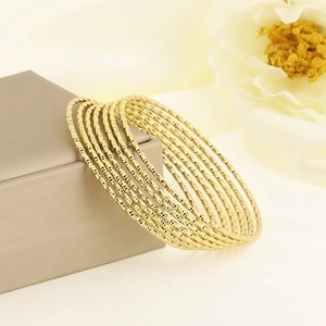Detail of stacked gold stainless steel bangles with textured diamond patterns on a box