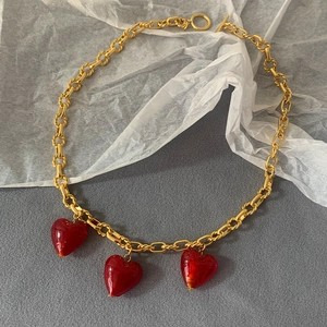 Detailed close-up of golden chunky chain necklace with three red Murano glass hearts