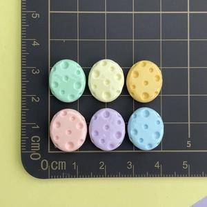 Miniature pastel oval resin charms with pitted texture on a black measurement grid