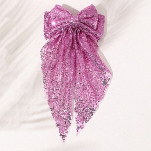 Detailed view of oversized pink sequin bow hair clip with long streamers on white surface