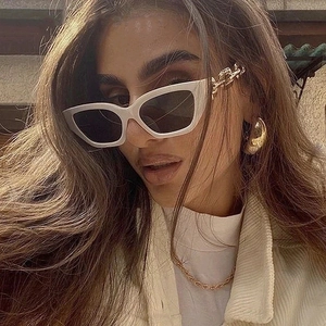 Close-up of white cat eye sunglasses with gold chain temples on model in sunlight