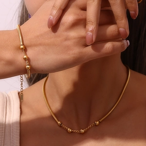 Detail view of gold bead snake chain necklace and bracelet set on model's neck and hand